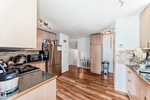Modern kitchen featuring wood-finish flooring, light wood cabinetry, stone-look countertops, and a full stainless steel appliance package - 1804 51 Street Nw, Edmonton, AB - Indoor Photo Showing Kitchen