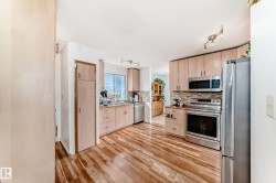 Kitchen featuring wood-finish flooring, light-toned cabinetry, a mosaic tile backsplash, and stainless steel appliances including an oven range, microwave, and refrigerator - 