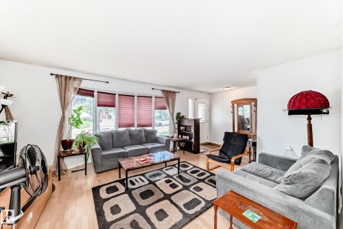 Bright main living area featuring light wood-finish flooring, a bay window with blinds, and white painted walls - 1804 51 Street Nw, Edmonton, AB - Indoor Photo Showing Living Room