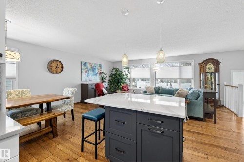 The open concept living area features hardwood floors, a kitchen island with a white countertop and pendant lighting, and large windows providing natural light - 17 Austin Crescent, St. Albert, AB - Indoor