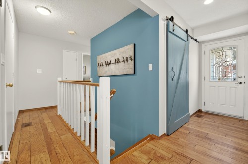 The property features natural wood flooring, a decorative barn door, and a white front door with an ornate glass insert - 17 Austin Crescent, St. Albert, AB - Indoor Photo Showing Other Room