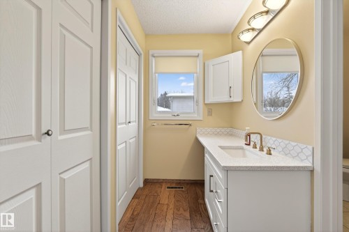 This bathroom features a contemporary vanity with a white countertop and an integrated sink, complemented by a gold-framed oval mirror and a three-light fixture - 17 Austin Crescent, St. Albert, AB - Indoor Photo Showing Bathroom