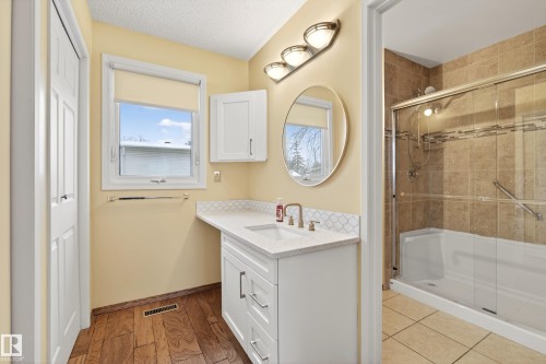 This bathroom features a vanity with a white countertop and brass-toned faucet, a window providing natural light, and a shower with a glass enclosure and tiled walls - 17 Austin Crescent, St. Albert, AB - Indoor Photo Showing Bathroom