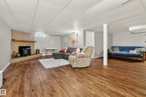 This spacious room features wood-look flooring and a fireplace with a brick surround and wooden mantel - 17 Austin Crescent, St. Albert, AB - Indoor With Fireplace