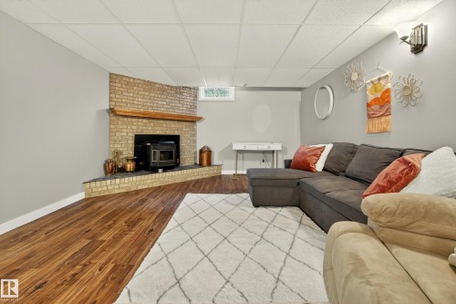 This living area features a brick fireplace with a wood mantle and a dark wood stove insert - 17 Austin Crescent, St. Albert, AB - Indoor Photo Showing Living Room With Fireplace