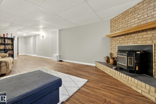 This spacious living area features wood flooring, light grey walls, and a brick fireplace with a decorative mantel and hearth - 17 Austin Crescent, St. Albert, AB - Indoor Photo Showing Living Room With Fireplace