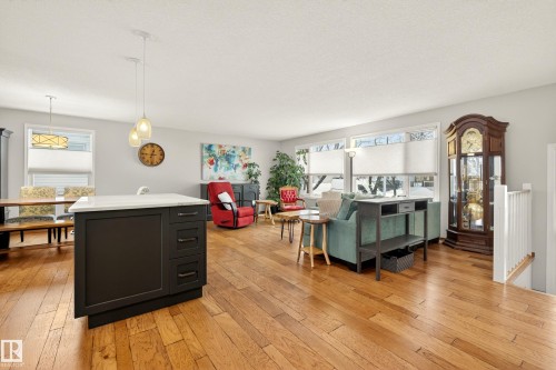 Open concept living area featuring hardwood flooring, a kitchen island with a white countertop and dark cabinetry, and large windows providing natural light - 17 Austin Crescent, St. Albert, AB - Indoor