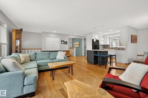 The property features hardwood flooring throughout this area, with an open-concept design that includes a kitchen with white cabinetry, black appliances, and a central island with seating - 17 Austin Crescent, St. Albert, AB - Indoor Photo Showing Living Room