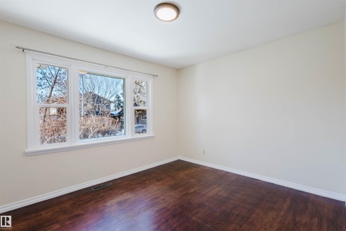 Bright room featuring a large multi-pane window with white trim, wood-finish flooring, light-toned walls, and a ceiling-mounted light fixture - 10511 80 Street, Edmonton, AB - Indoor Photo Showing Other Room