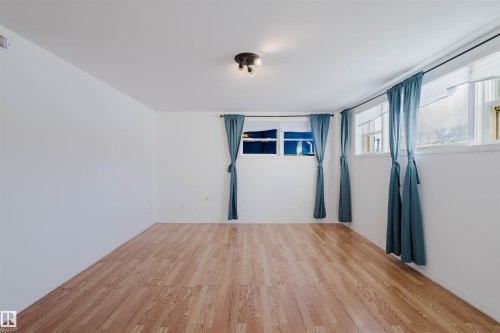 Spacious room featuring wood-finish flooring, white walls, multiple windows, and a flush-mount ceiling light fixture - 10511 80 Street, Edmonton, AB - Indoor Photo Showing Other Room