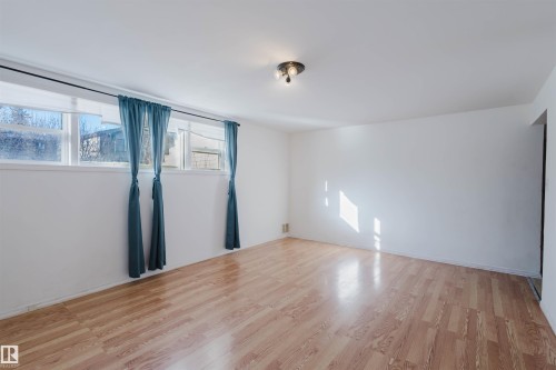 Spacious room featuring wood-finish flooring, white walls, multiple windows, a ceiling-mounted light fixture, and baseboard trim - 10511 80 Street, Edmonton, AB - Indoor Photo Showing Other Room