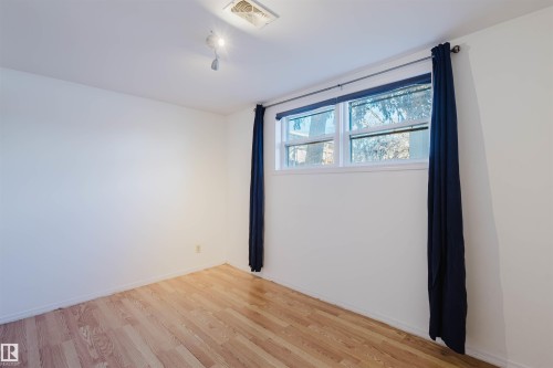 Room featuring wood-finish flooring, white walls, and a window with a roller shade and dark drapery panels - 10511 80 Street, Edmonton, AB - Indoor Photo Showing Other Room