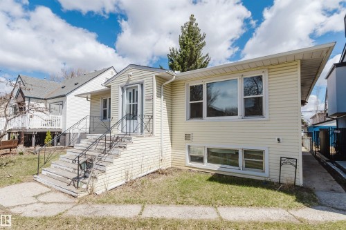 Yellow siding exterior with white trim, featuring multiple windows and a front entrance with a screen door and wrought iron railings - 10511 80 Street, Edmonton, AB - Outdoor