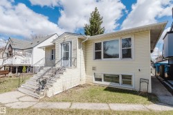 Yellow siding exterior with white trim, featuring multiple windows and a front entrance with a screen door and wrought iron railings - 