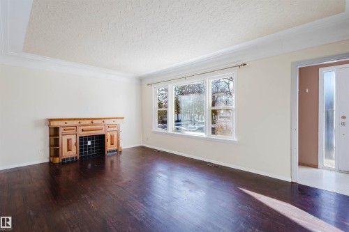 Spacious interior featuring dark wood-finish flooring, a decorative fireplace with wood cabinetry and black tile surround, and an expansive window providing natural light - 10511 80 Street, Edmonton, AB - Indoor Photo Showing Living Room