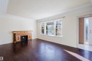 Spacious interior featuring dark wood-finish flooring, a decorative fireplace with wood cabinetry and black tile surround, and an expansive window providing natural light - 10511 80 Street, Edmonton, AB  - Indoor Photo Showing Living Room 