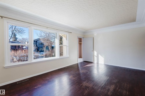 Expansive window wall with multiple panes, dark wood-finish flooring, white crown molding, and a neutral wall palette - 10511 80 Street, Edmonton, AB - Indoor Photo Showing Other Room