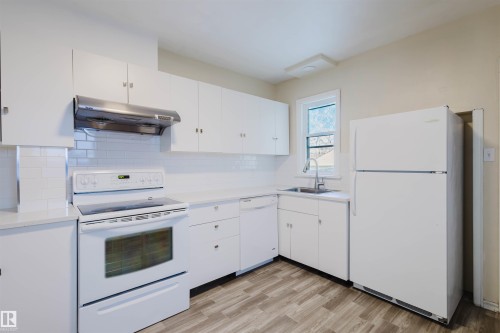 Kitchen featuring white cabinetry, white subway tile backsplash, light-toned countertops, wood-finish flooring, and a stainless steel range hood - 10511 80 Street, Edmonton, AB - Indoor Photo Showing Kitchen