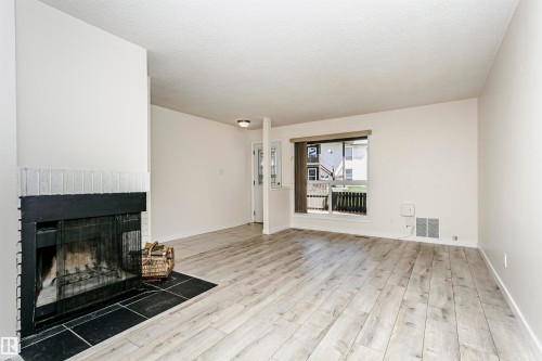 Spacious living area featuring wood-finish flooring, a fireplace with a black tile hearth, and a window with natural light - 9221 172 Street, Edmonton, AB - Indoor Photo Showing Living Room With Fireplace