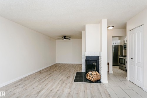 Living area featuring a fireplace with a white brick surround and black hearth, wood-finish flooring, and a ceiling fan - 9221 172 Street, Edmonton, AB - Indoor Photo Showing Other Room With Fireplace