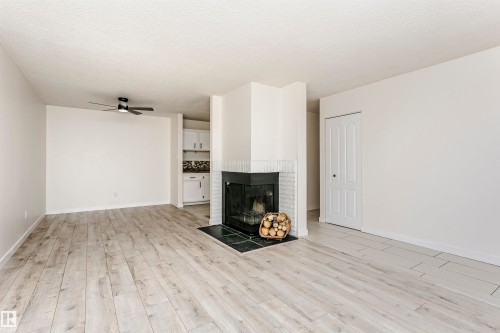 Spacious interior featuring wood-finish flooring, a fireplace with a black surround and white brick hearth, and a ceiling fan - 9221 172 Street, Edmonton, AB - Indoor Photo Showing Other Room With Fireplace