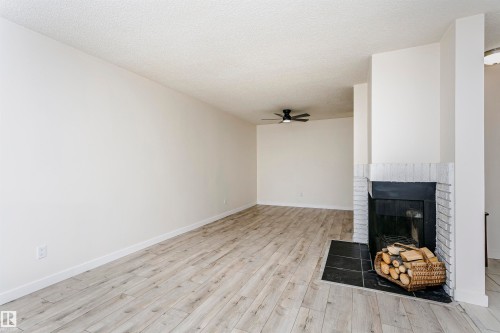 Living area featuring wood-finish flooring, a white brick fireplace with a black hearth, a black ceiling fan, and white painted walls - 9221 172 Street, Edmonton, AB - Indoor With Fireplace