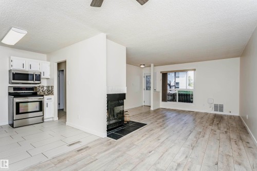 Living area featuring wood-finish flooring, a fireplace with a dark stone hearth, a large window, and a ceiling fan - 9221 172 Street, Edmonton, AB - Indoor