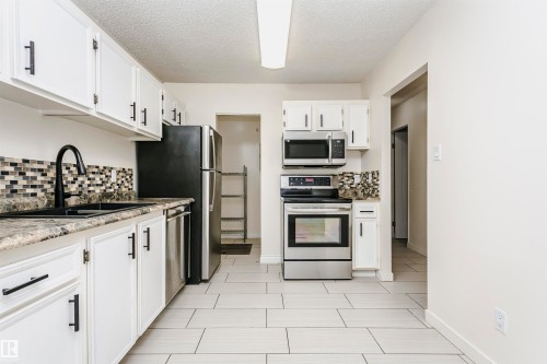 Kitchen featuring white cabinetry with matte black hardware, stainless steel appliances, mosaic tile backsplash, and light-toned tile flooring - 9221 172 Street, Edmonton, AB - Indoor Photo Showing Kitchen With Stainless Steel Kitchen