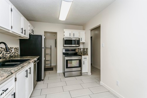 Kitchen featuring white cabinetry with black hardware, mosaic tile backsplash, black sink with gooseneck faucet, light-toned tile flooring, and stainless steel appliances - 9221 172 Street, Edmonton, AB - Indoor Photo Showing Kitchen With Stainless Steel Kitchen With Double Sink