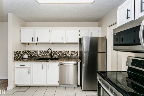 Kitchen featuring white cabinetry with black hardware, mosaic tile backsplash, dark-finish countertops, stainless steel appliances, and large format tile flooring - 9221 172 Street, Edmonton, AB - Indoor Photo Showing Kitchen With Stainless Steel Kitchen