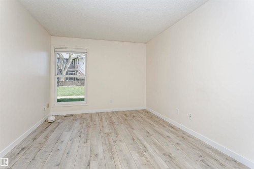 Bright room featuring wood-finish flooring, crisp white walls, and a large window with blinds - 9221 172 Street, Edmonton, AB - Indoor Photo Showing Other Room