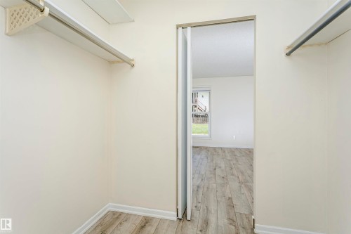 Walk-in closet featuring light wood-finish flooring, white walls, and built-in shelving with hanging rods - 9221 172 Street, Edmonton, AB - Indoor With Storage