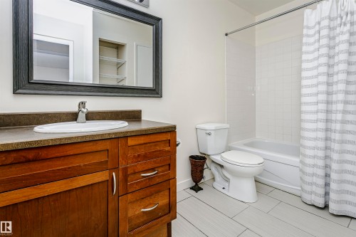 Bathroom featuring a wood-finish vanity with a surface-mount sink, a framed wall mirror, a full-size bathtub with subway tile surround, and light-tone plank flooring - 9221 172 Street, Edmonton, AB - Indoor Photo Showing Bathroom