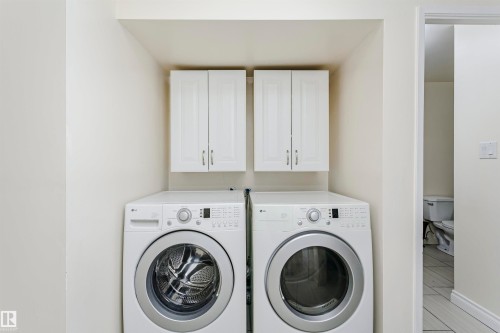 Dedicated laundry area featuring a front-loading washer and dryer set, complemented by two white upper cabinets for storage - 9221 172 Street, Edmonton, AB - Indoor Photo Showing Laundry Room