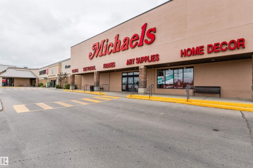 Retail storefront featuring a tan facade with red signage, multiple display windows, and a black metal bench - 9221 172 Street, Edmonton, AB - Outdoor