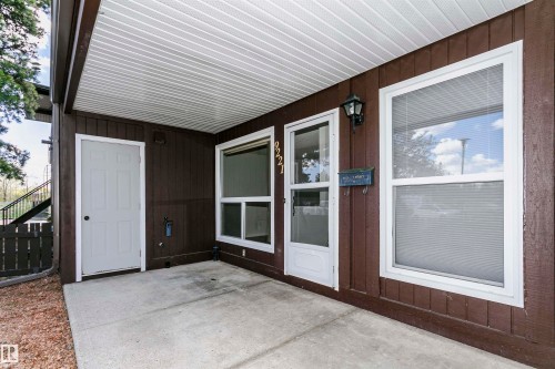 Covered concrete patio entrance featuring brown siding, white trim windows, and a dedicated storage door - 9221 172 Street, Edmonton, AB - Outdoor With Exterior