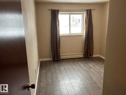 This room features hardwood flooring, a window with natural light, and neutral-toned walls - 4 10164 150 Street, Edmonton, AB - Indoor Photo Showing Other Room