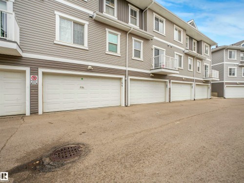 Multi-level townhouse exterior featuring horizontal siding in a neutral tone, white-trimmed windows, multiple white garage doors, and individual white balconies with railings - 44 1140 Chappelle Boulevard, Edmonton, AB - Outdoor With Exterior