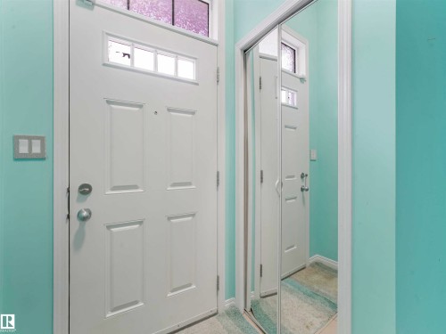 Entryway featuring a white paneled door with glass inserts and a transom window, complemented by a mirrored closet door - 44 1140 Chappelle Boulevard, Edmonton, AB - Indoor Photo Showing Other Room