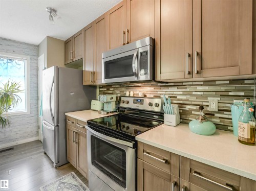 Modern kitchen featuring light wood-finish cabinetry, stainless steel appliances, a multi-tone linear tile backsplash, and light-toned countertops - 44 1140 Chappelle Boulevard, Edmonton, AB - Indoor Photo Showing Kitchen With Stainless Steel Kitchen
