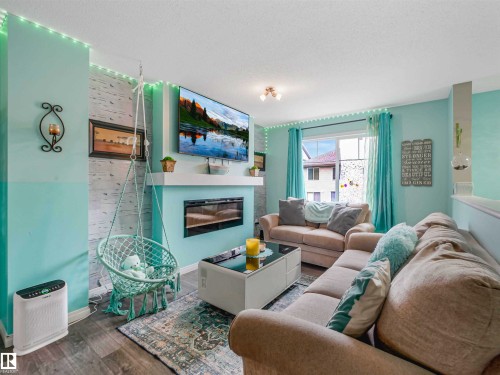Living area with a built-in electric fireplace and mantel, wood-finish flooring, and a sliding glass door - 44 1140 Chappelle Boulevard, Edmonton, AB - Indoor Photo Showing Living Room With Fireplace