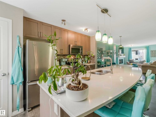 Kitchen featuring a large curved island with an undermount sink and bar seating, stainless steel appliances, and wood-finish cabinetry - 44 1140 Chappelle Boulevard, Edmonton, AB - Indoor Photo Showing Kitchen With Stainless Steel Kitchen With Double Sink With Upgraded Kitchen