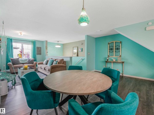 Open-concept living space featuring wood-finish flooring, a round dining table, a decorative pendant light, a window with natural light, and a partial view of an upper-level railing - 44 1140 Chappelle Boulevard, Edmonton, AB - Indoor