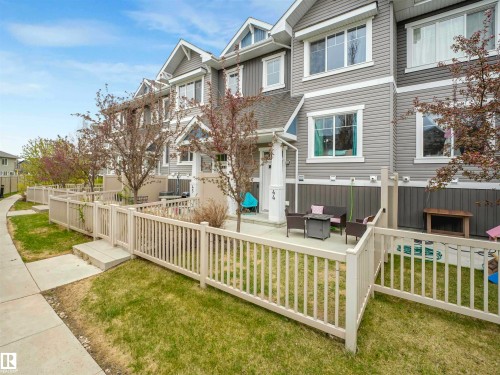 Multi-level townhome exterior featuring gray siding with white trim, a private patio, and a fenced front yard with mature trees - 44 1140 Chappelle Boulevard, Edmonton, AB - Outdoor