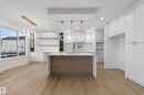 Modern kitchen featuring a waterfall-edge island with wood-finish paneling, white shaker cabinetry, and light wood-finish flooring - 4276 Charles Close, Edmonton, AB  - Indoor Photo Showing Kitchen 