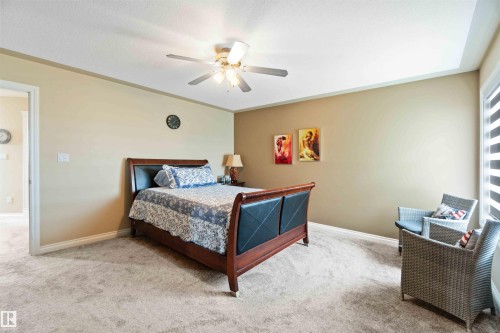 Carpeted room featuring a ceiling fan with integrated lighting, a tray ceiling, and a window with horizontal blinds - 6116 53 Avenue, Beaumont, AB - Indoor Photo Showing Bedroom