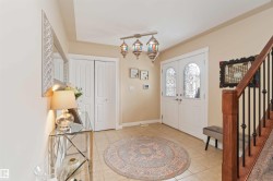 Entryway featuring double doors with decorative glass panels, tile flooring, a built-in closet, a wooden staircase with black iron balusters, and a unique multi-light fixture - 