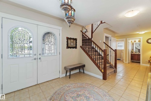 Entryway featuring double doors with decorative glass panels, a tiled floor, and a staircase with wood newel posts and metal balusters - 6116 53 Avenue, Beaumont, AB - Indoor Photo Showing Other Room