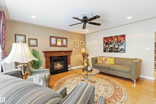 Living area featuring wood-finish flooring, a fireplace with a wood mantle and dark stone surround, and a ceiling fan with integrated lighting - 6116 53 Avenue, Beaumont, AB - Indoor Photo Showing Living Room With Fireplace