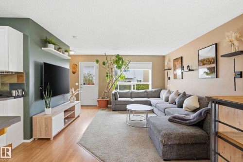 Open-concept living area featuring light wood-finish flooring, a large window, a white paneled door with glass inserts, and a kitchen pass-through with white cabinetry and a stone tile backsplash - 14017 156 Avenue, Edmonton, AB - Indoor Photo Showing Living Room